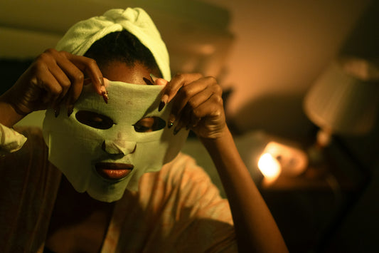 A woman applying a fabric sheet mask to her face in warm evening light