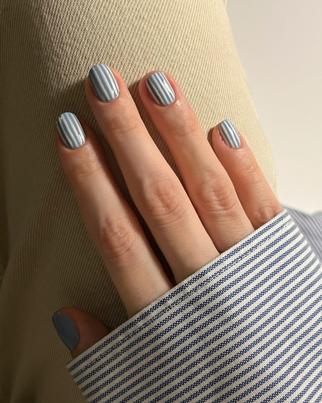 A hand with pale blue and white pinstripe nail art resting on fabric
