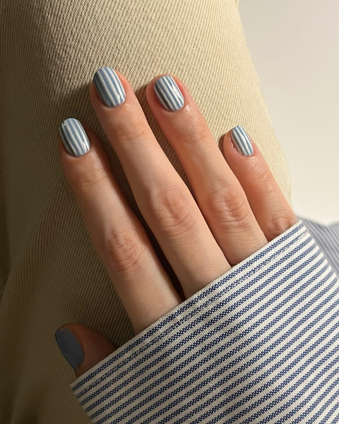 A hand with pale blue and white pinstripe nail art resting on fabric